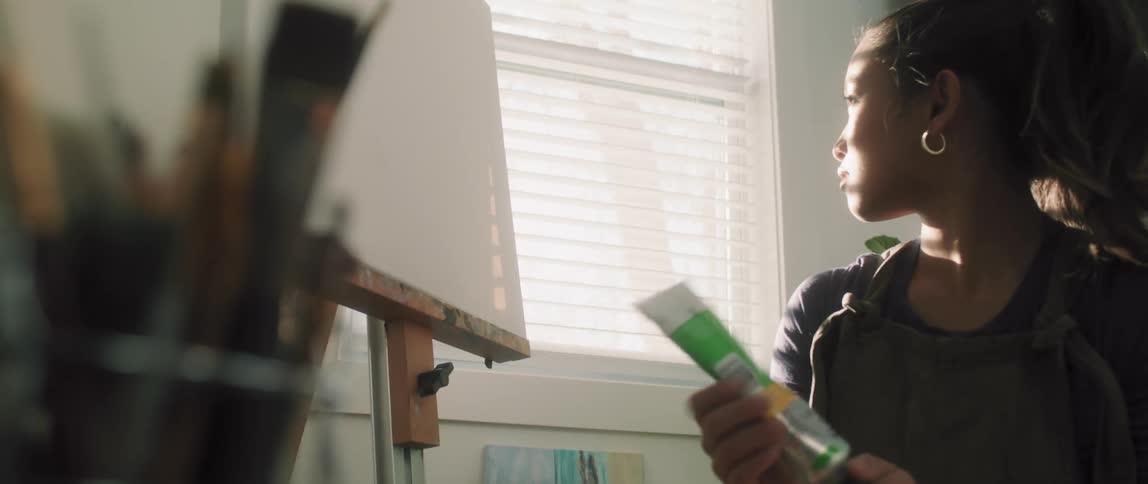 Young woman pouring oil paint on a pallet over a table in a studio