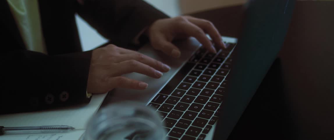 A person working in an office closes a laptop and starts writing in a notepad