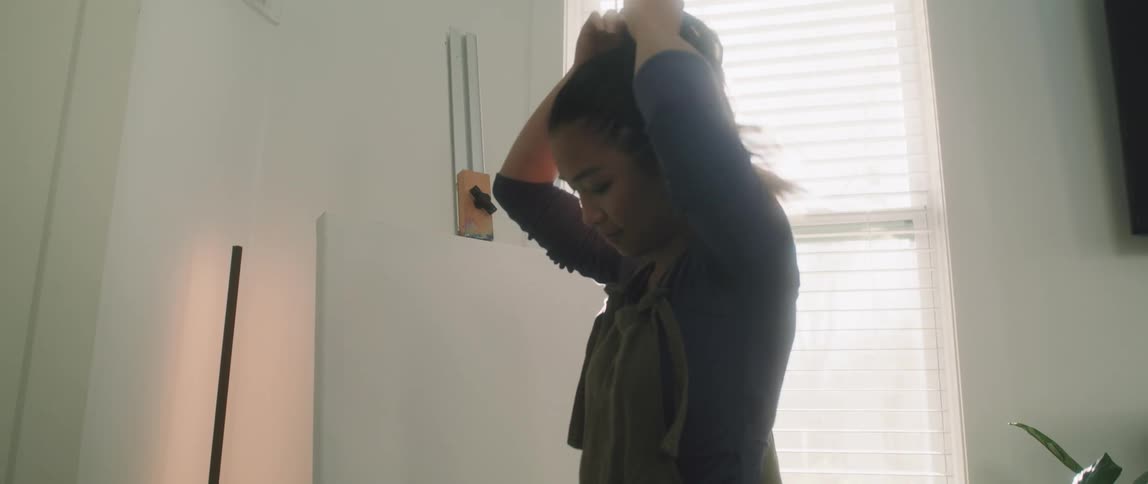 A woman in a room tying her hair then picking up a paint palette and opening paint