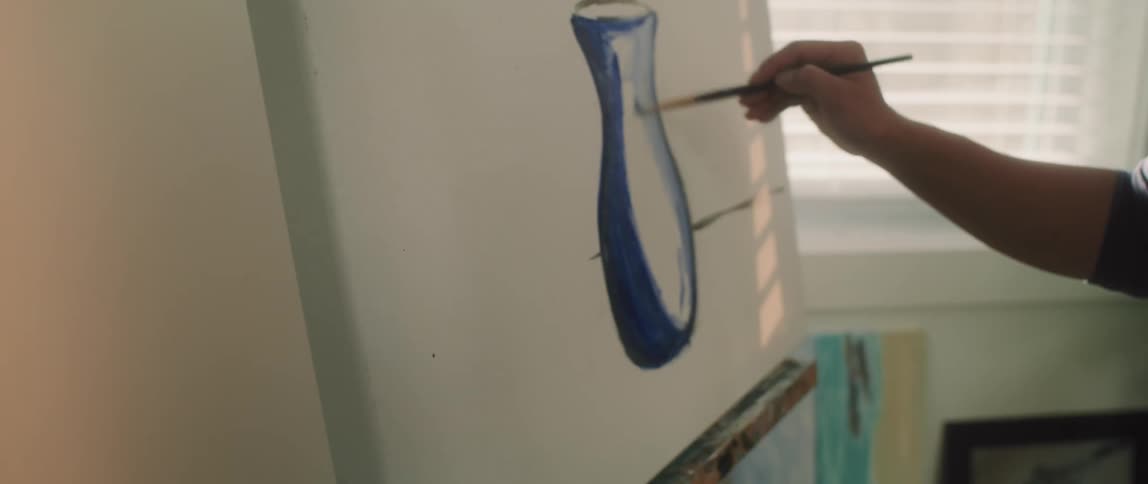 An asian girl stands at an easel painting a blue vase