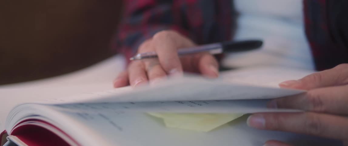 Woman holding pen pages through book smiling