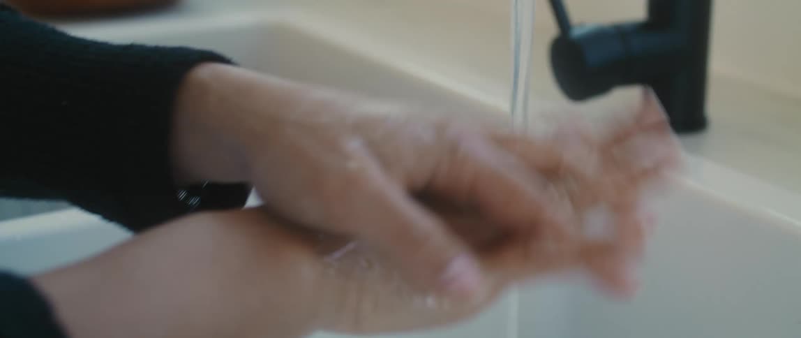 An asian female teenager washes her hands with soap at a white sink in front of a window