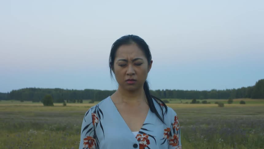 Young asian woman with eyes closed screams angrily while standing in a wide open field