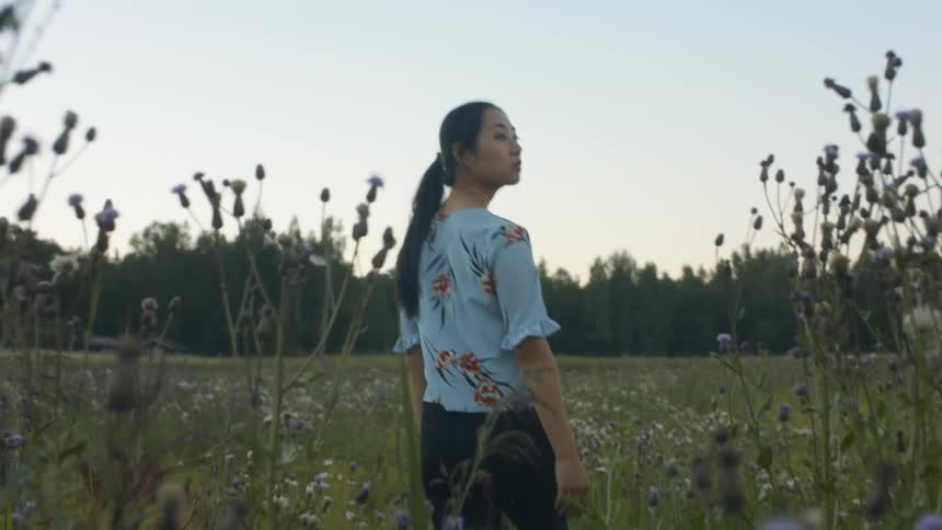 A young woman walks through a field of flowers and looks around