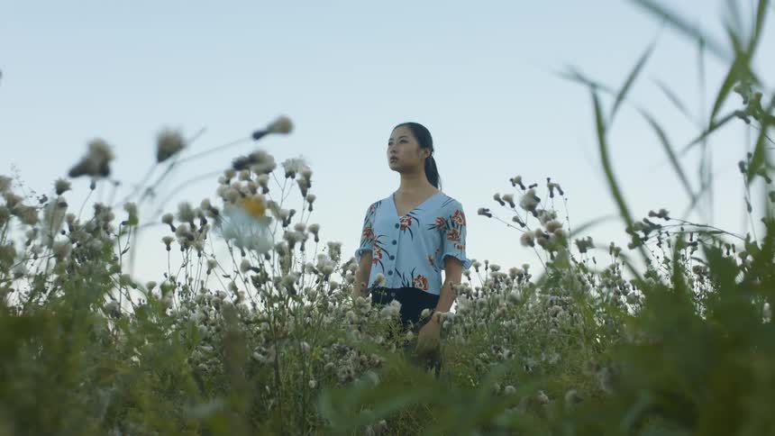 A young woman stands in a field of flowers and looks around