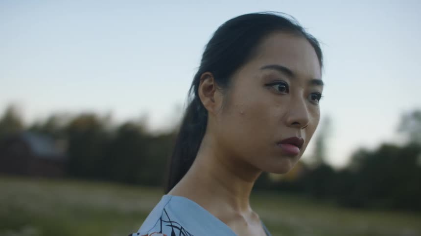A woman stands outside in a field looking around while the sun is low in the sky