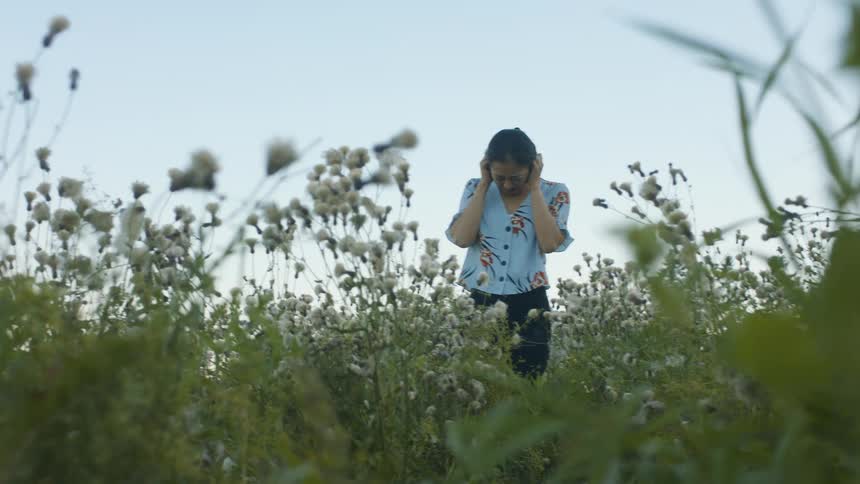 Woman standing in a field of flowers clenching her fist to her face