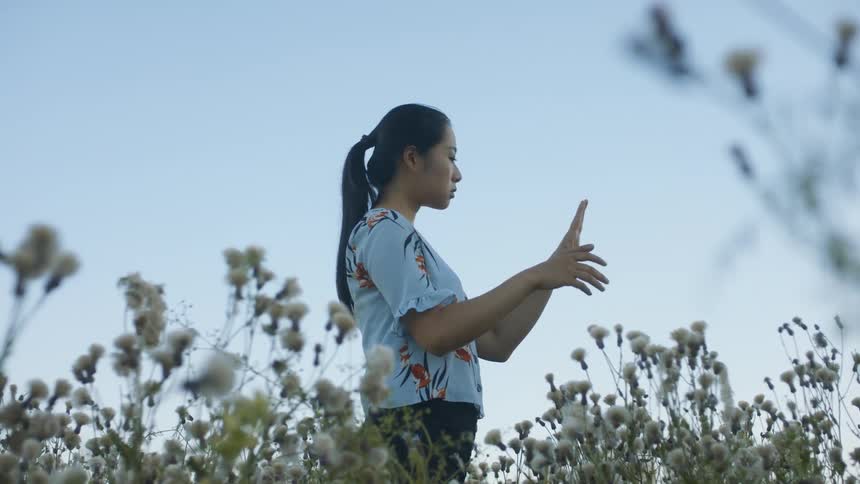 A woman stands out in a field moving her arms and hands