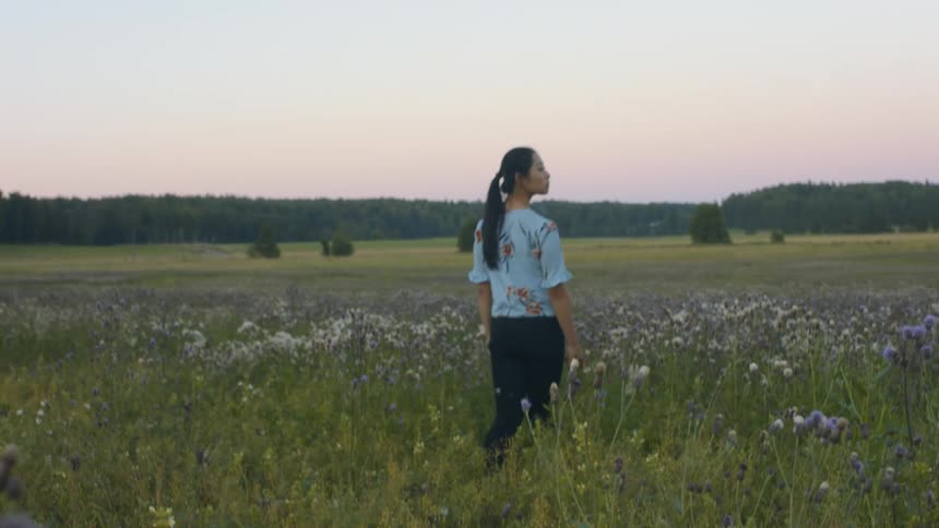 A woman is walking through a field of flowers at dusk