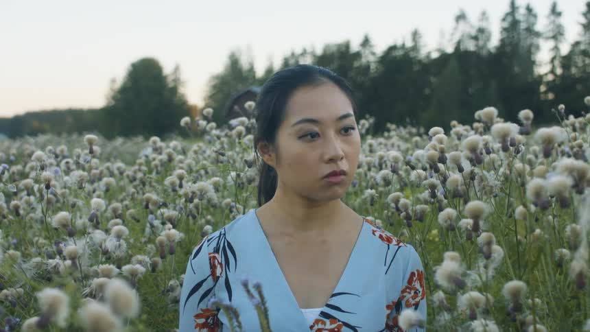 A woman stands in a field while looking off into the distance