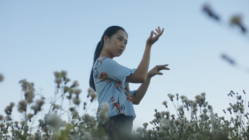 A young woman standing in a field looks at her arms with confusion