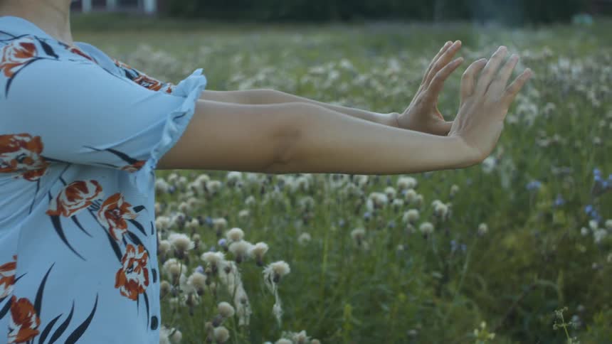 A young woman stands in a field of flowers in a rural area and stretches her arms out in front of her