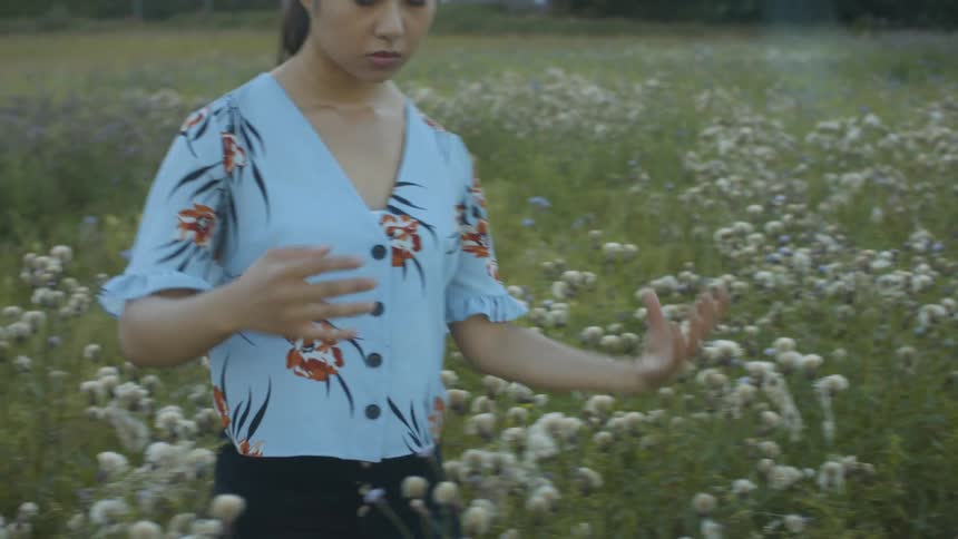 A woman is making movements with her arms as she stands outside in a field with flowers in front of a house
