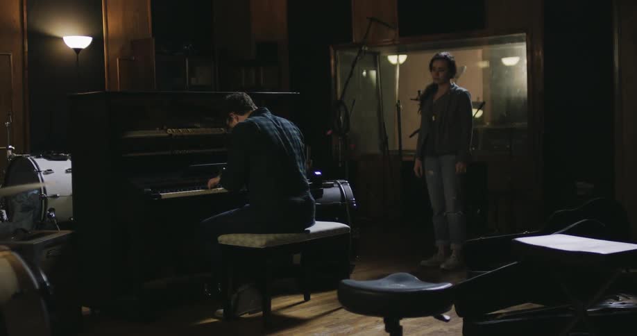 A woman walks over to a man playing the piano