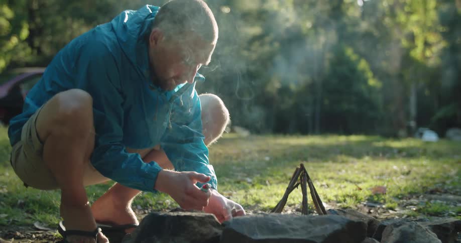 A man lights a stone ringed campfire with a lighter and some kindling