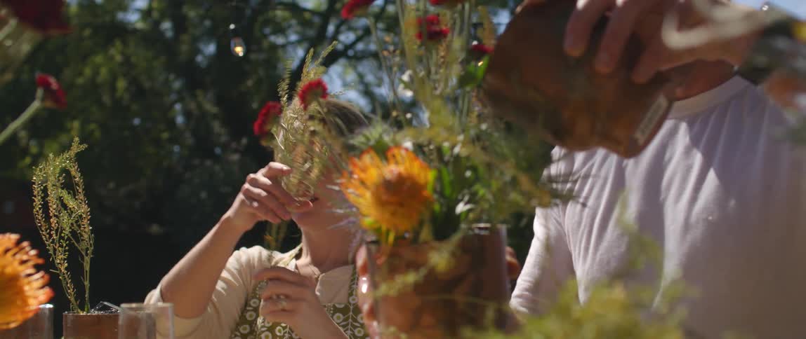 Man and woman arrange flowers outside under clear blue sky