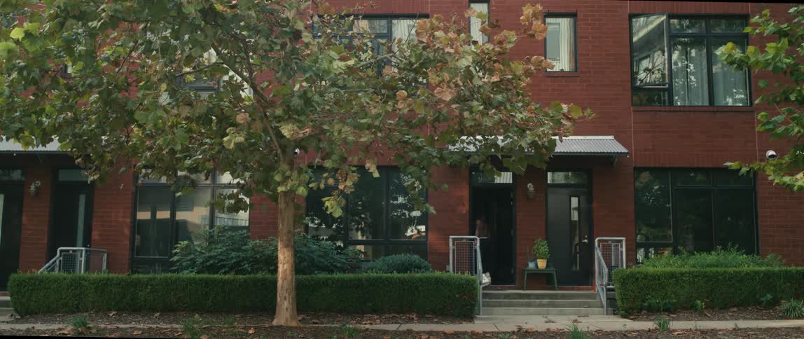A shirtless man roller blades up to his apartment building and enters