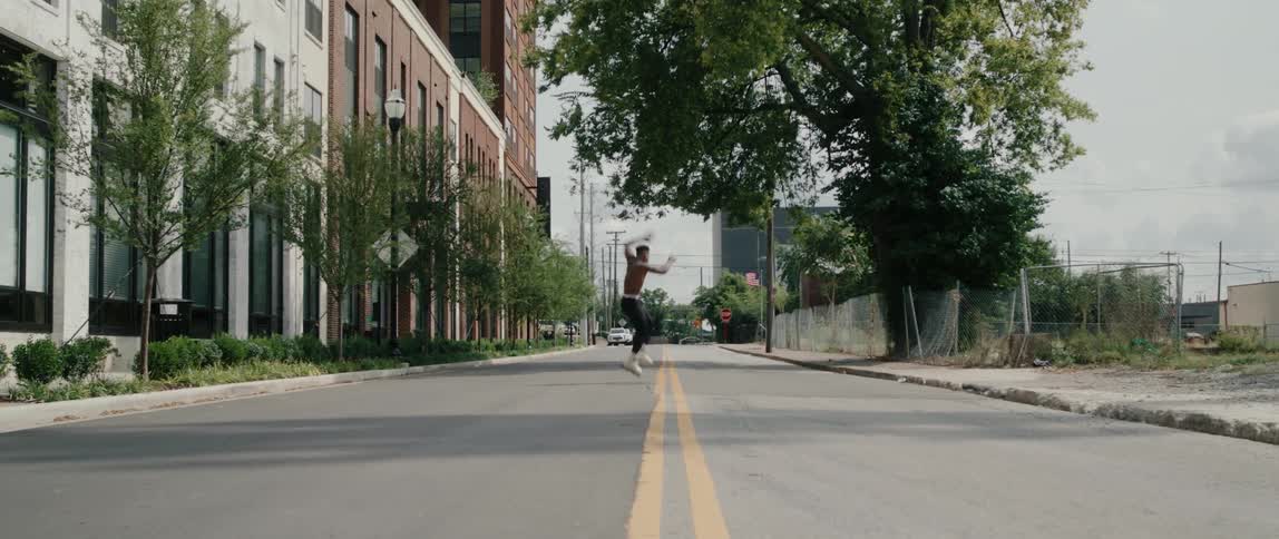 A shirtless man jumping and doing a full rotation while rollerblading on a city street