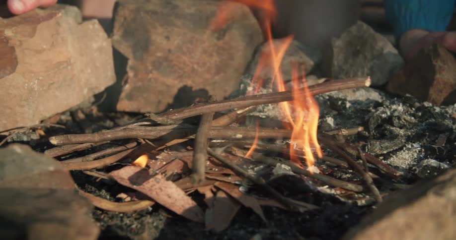 A person adds sticks to the fire in a campfire outdoors at day time