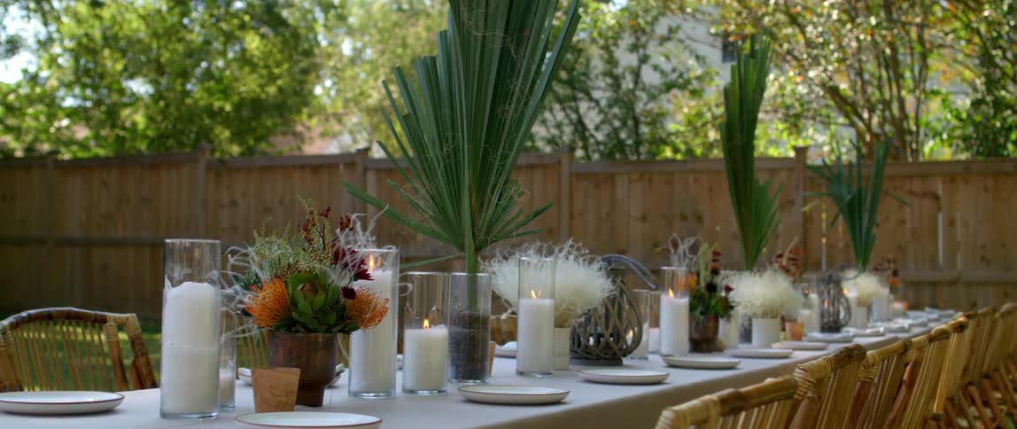 Dining table set up with candles plates and decorations outdoors in a backyard at daytime