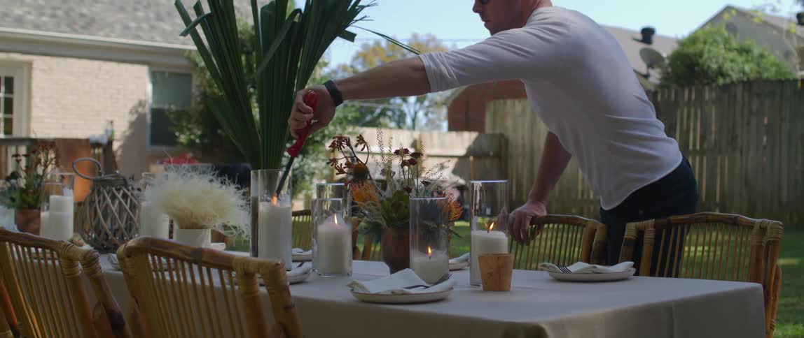 Man lighting candles at a dining room table set up in a backyard at daytime