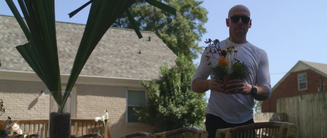 Man placing flower arrangements over the tables in the backyard at home