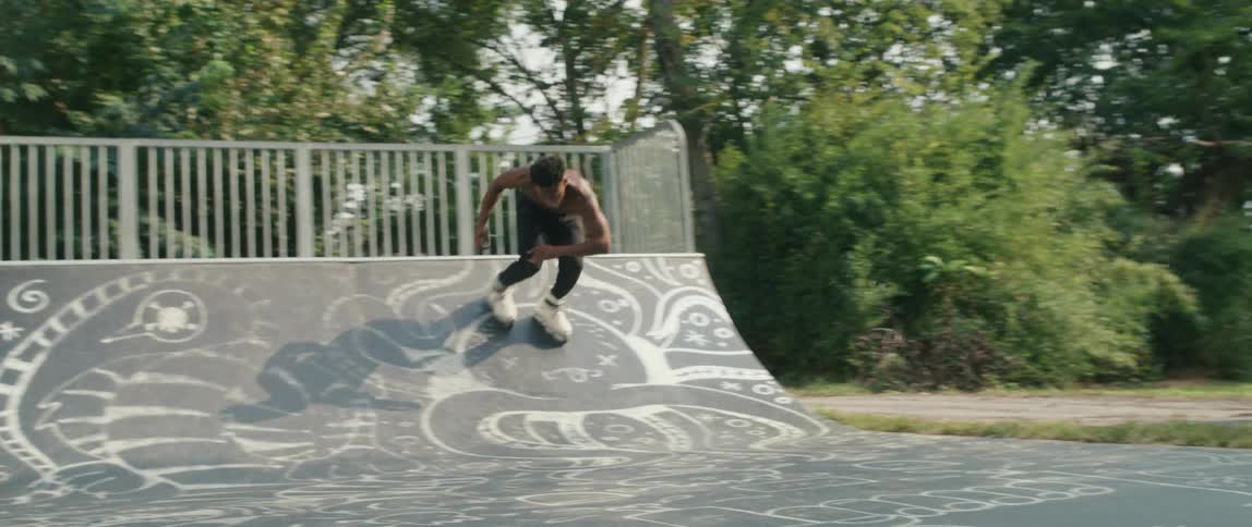 A black male teenager rollerblades in a parking lot with ramps