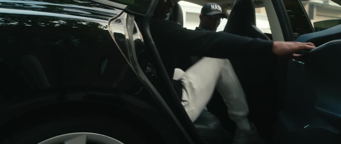 A teenager gets into the back seat of a black sports car on the side of a street
