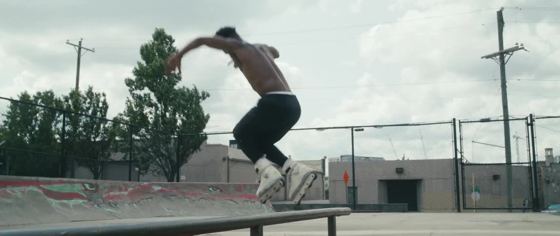 A man with in line skates skating in a skate park with trees buildings the sky and clouds in the background