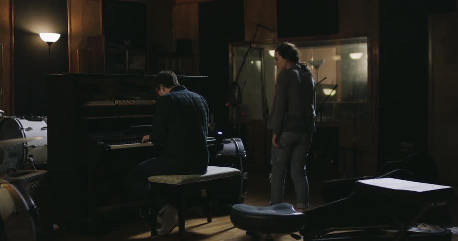 A man plays piano while a woman stands and walks up to him