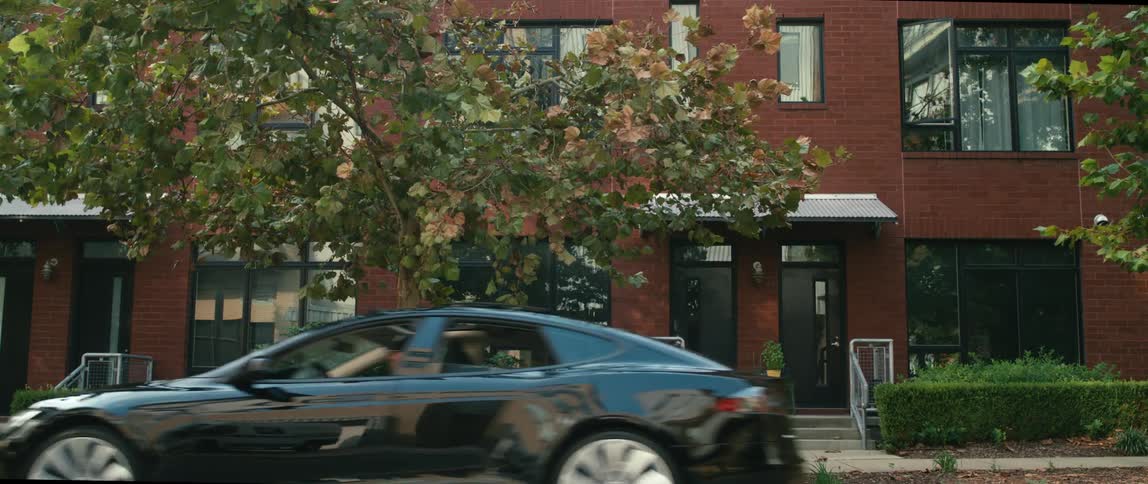 Man drives away in a black car from in front of a building