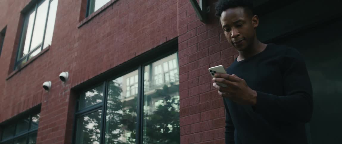 A smiling man walking out a building with a suitcase and smartphone