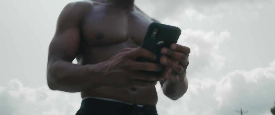 Shirtless black man using his smartphone and shouting at someone
