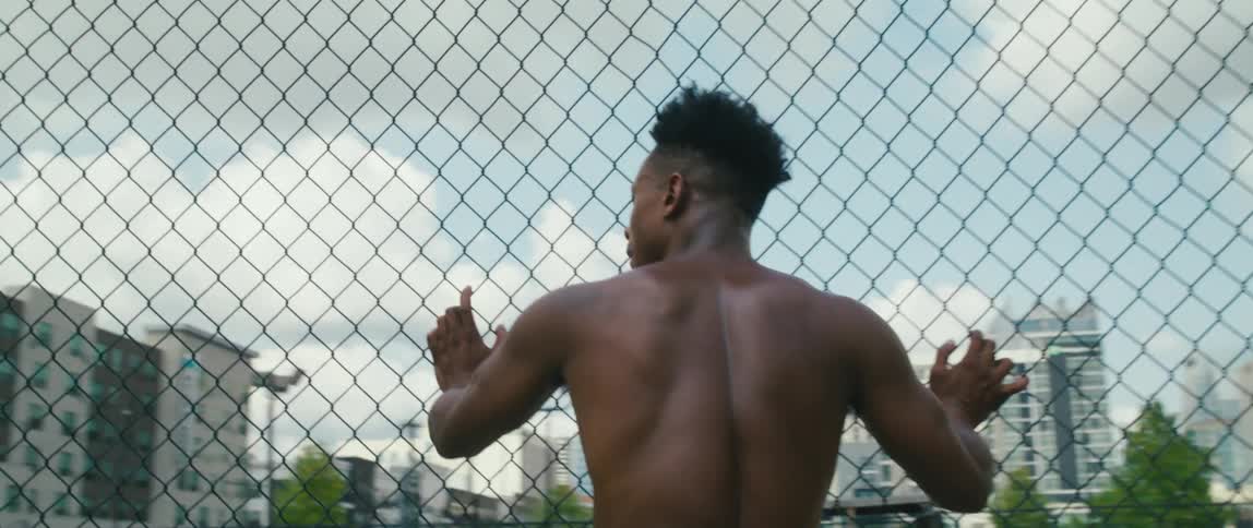 A black man rollerskating toward a fence and looking out at the city