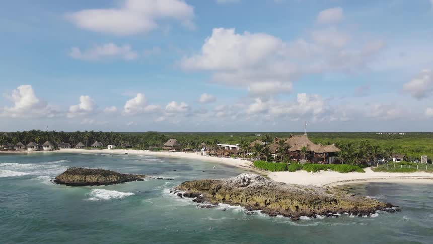 A sandy beach lined with houses on a flat landmass covered in forest on a sunny day