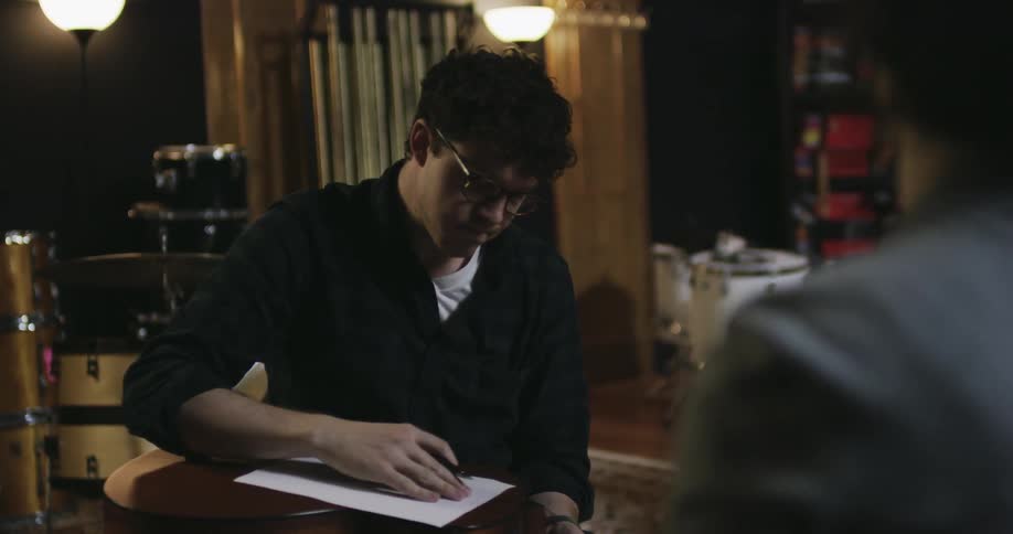 A man puts a guitar on his lap then writes on some paper