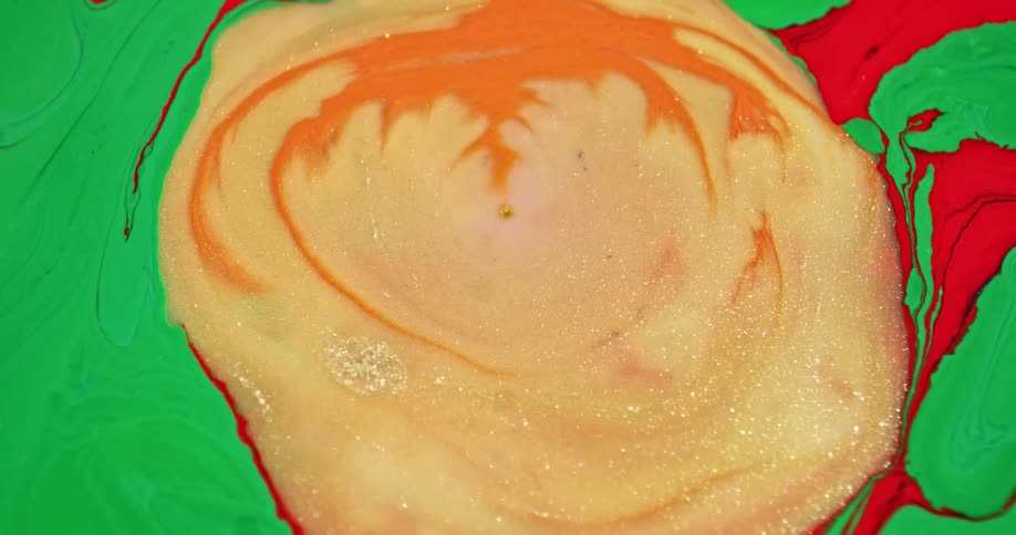 Liquid colorful bright gold ink flowing over orange and green ink forming abstract patterns