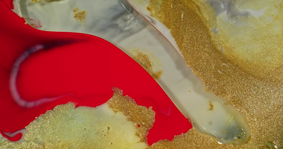 Bright red liquid ink pouring over golden glitter ink flowing over a surface