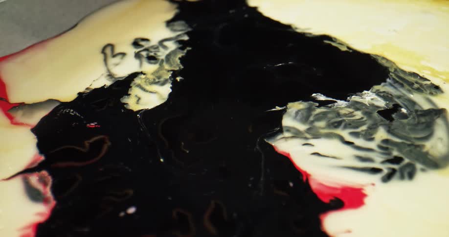 Black paint like liquid spreading on a cream colored surface with red and yellow