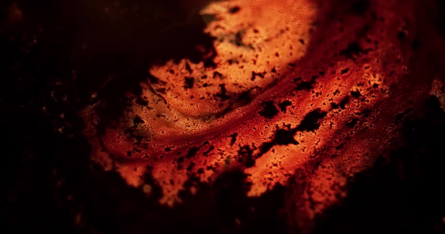 Light glows from under the surface of orange lava seeping out from black soot