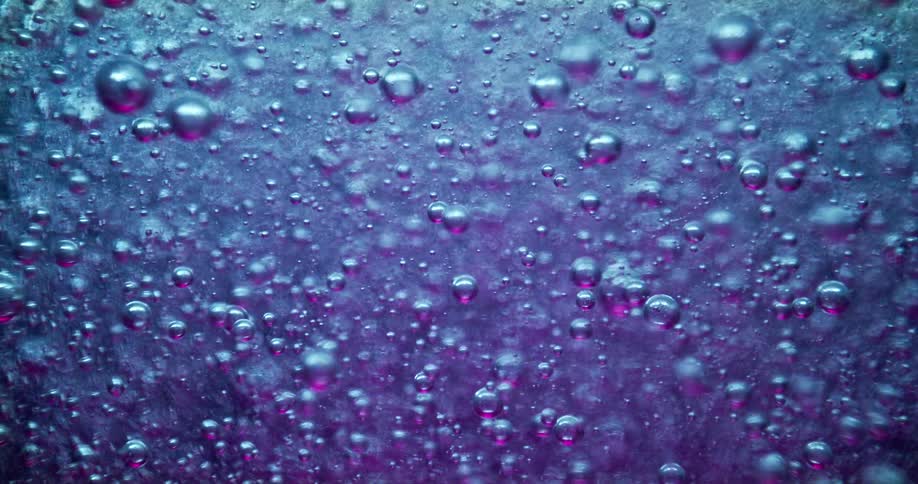 Air bubbles surfacing on a thick blue liquid with purple backlight
