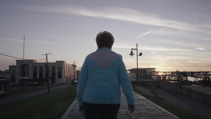 Woman walking a sidewalk towards the sunset