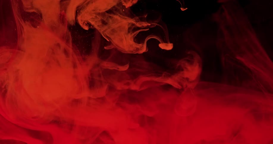 An opaque liquid is poured into a clear liquid as a eerie red hue is cast upon both