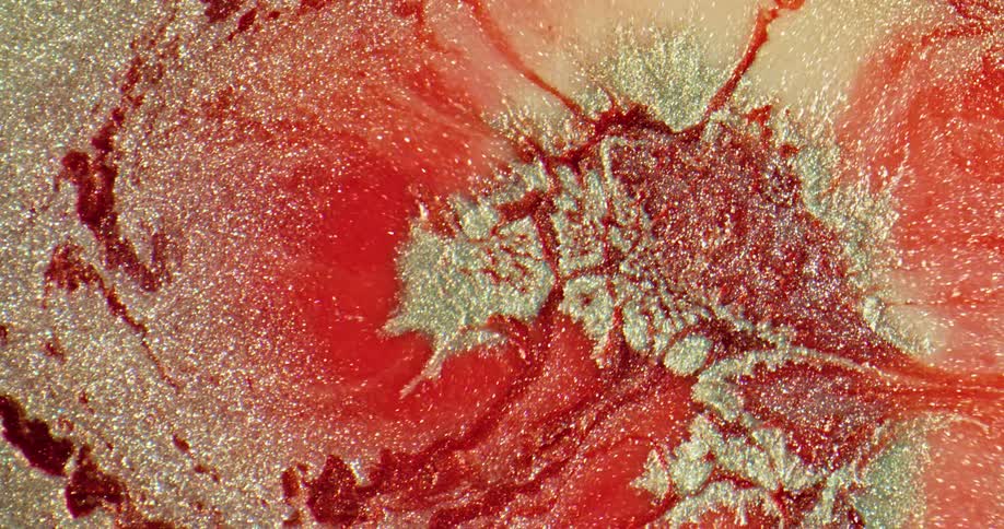 A red liquid moves outwards under a close up with silver particles