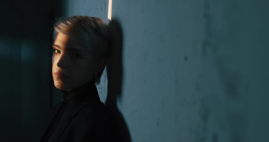 A woman standing in front of a dark wall with a light streak going down her face