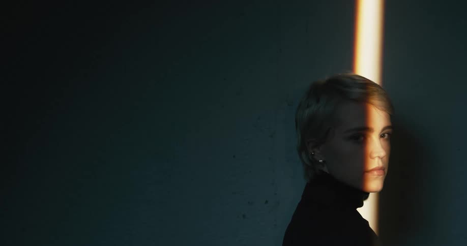 Young woman standing in a dimly lit room turns around to look at the camera