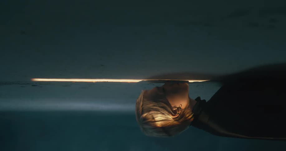 Woman presses her face against a thin beam of light on a wall then turns to look at the camera