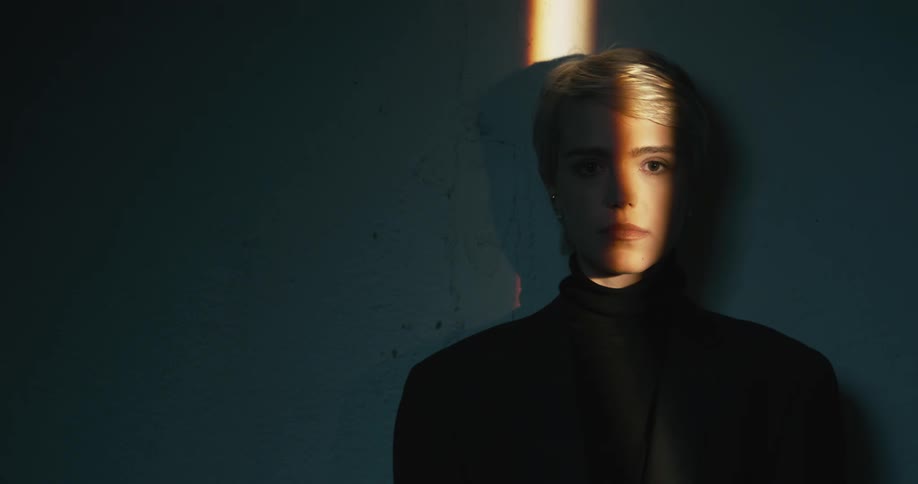 Young short haired blonde woman modeling looks at the camera inside a dimly lit room