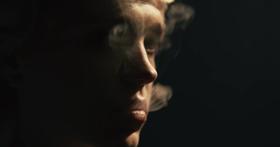 Close up of smoke coming out of a young womans face in a dark room
