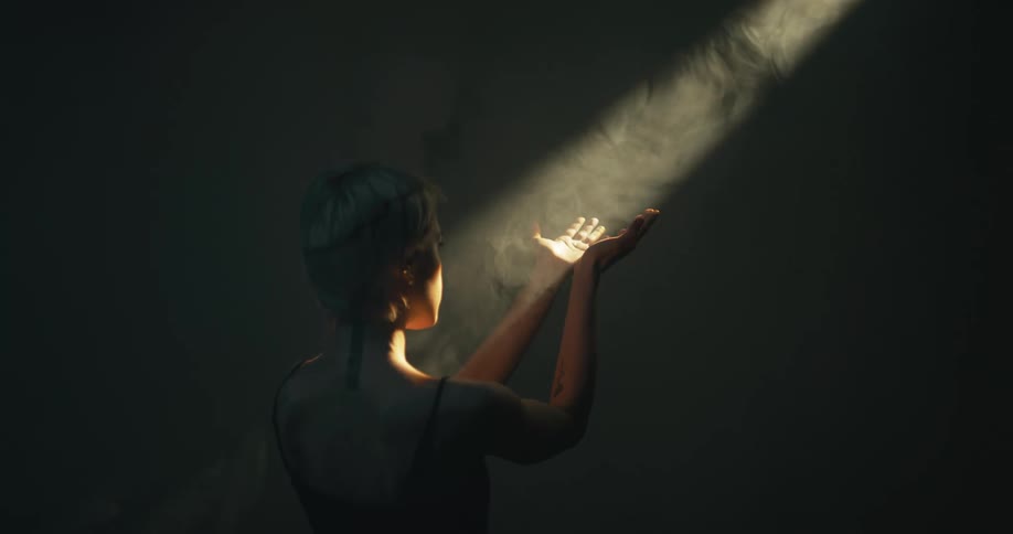 A woman standing in a room playing with a sunbeam with her hands